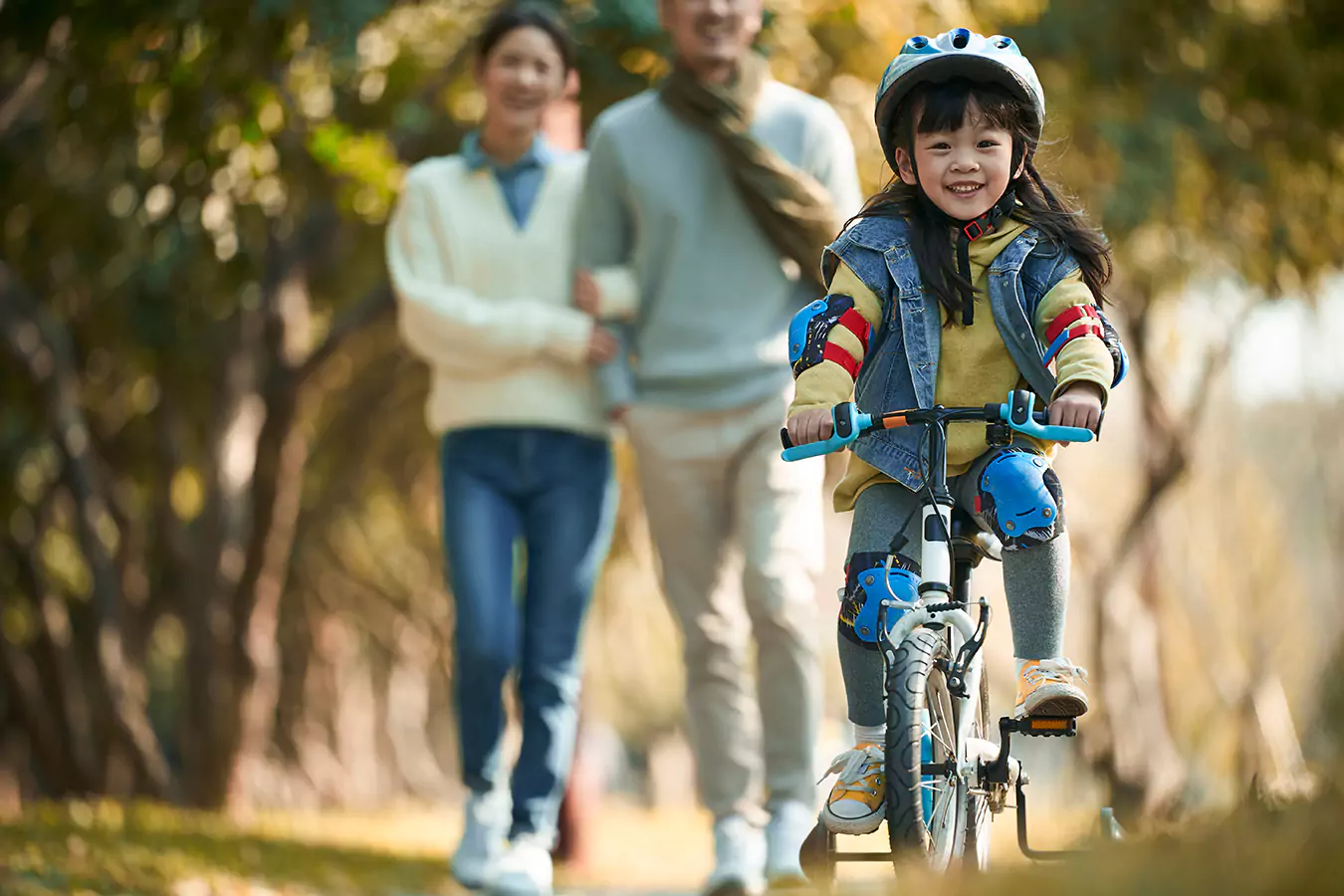 A girl riding the bicycle and her parents behind her